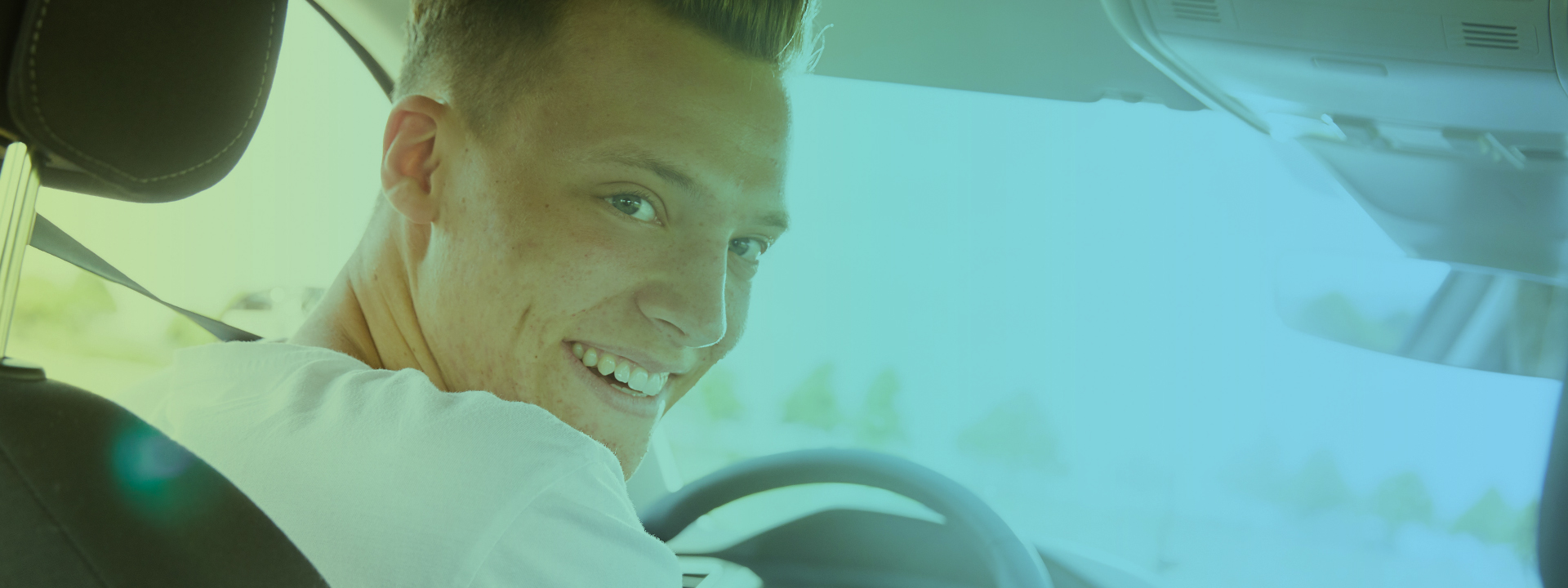 Junger Mann im Auto, lachend, Blick nach hinten auf Rücksitzbank